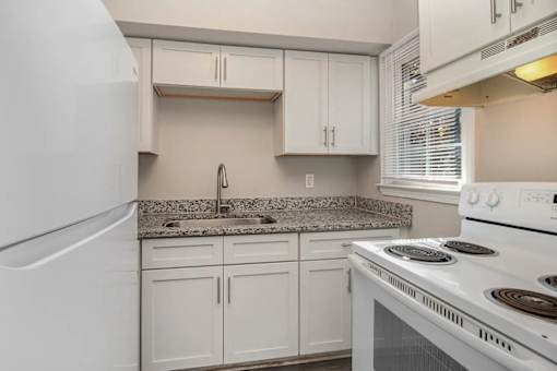 A white kitchen with a stove, sink, and cabinets.