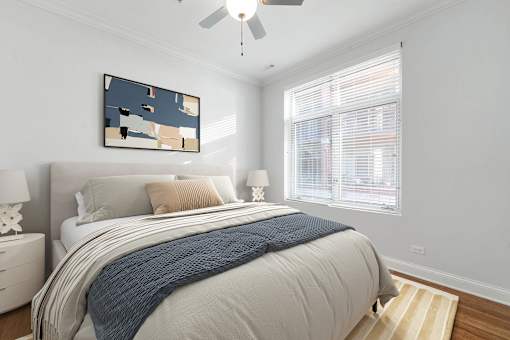A bedroom with a bed, pillows, a ceiling fan, and a painting on the wall.