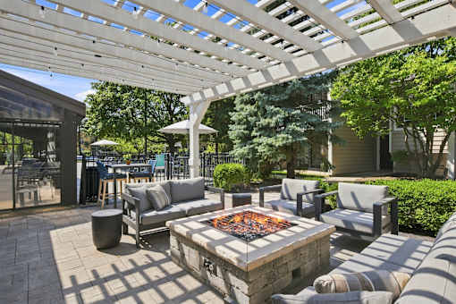 A patio with a fire pit and seating area under a white pergola.