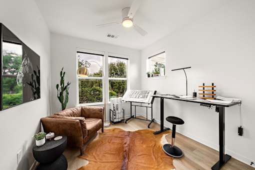 A room with a brown leather couch, a black stool, a white desk, and a brown rug.