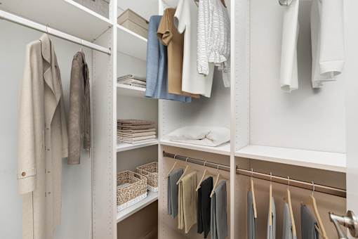 A white closet with clothes hanging on hangers.