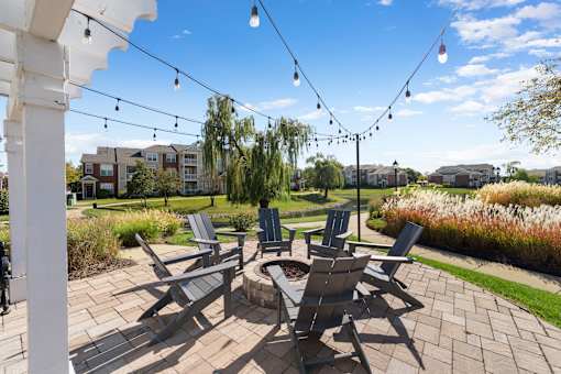 A patio with chairs and a table is surrounded by a garden.