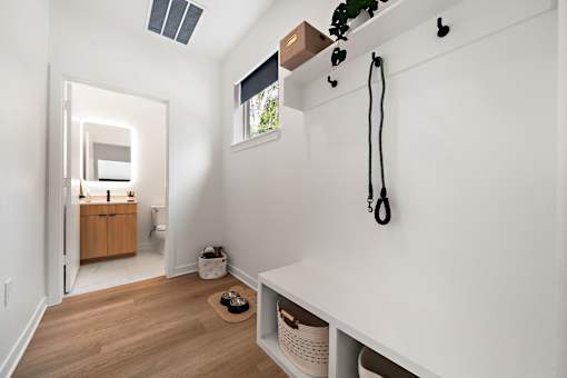 A white room with a wooden floor and a white wall with a black plant hanger on it.