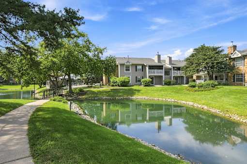 A serene lakeside walkway leads to a row of houses.