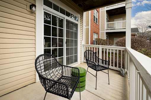 Two black chairs and a green stool are on a porch.