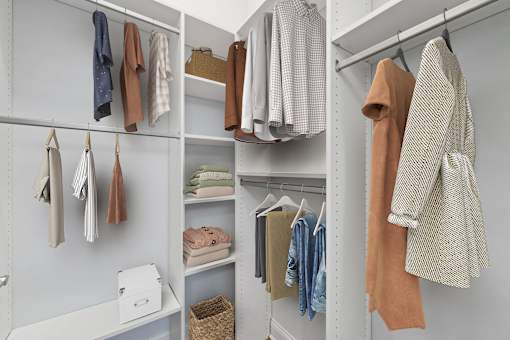 A white closet with clothes hanging and shelves.