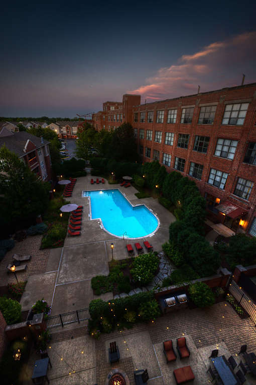 A pool surrounded by a patio with chairs and umbrellas.