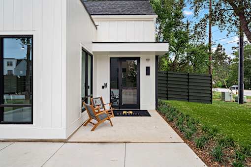 A white house with a black roof and a wooden chair in front.