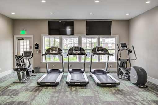 a gym with four treadmills and a tv on the wall