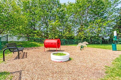 a fenced in play area with a red barrel and other playground equipment
