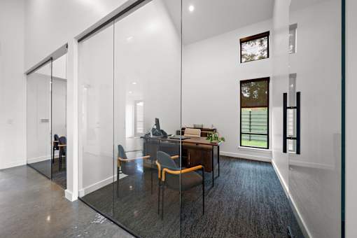 A modern home office with a glass wall and a desk with a chair.