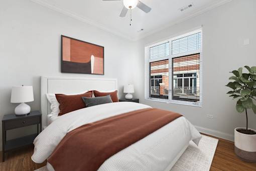 A bedroom with a large bed, a ceiling fan, and a potted plant.