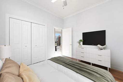 A white bedroom with a bed, a television, and a lamp.