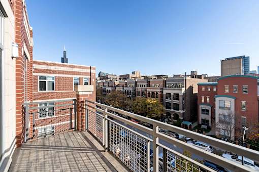 A balcony with a metal railing overlooks a parking lot and buildings.