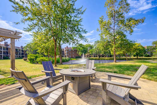 An outdoor firepit and chair next to a community grilling area.