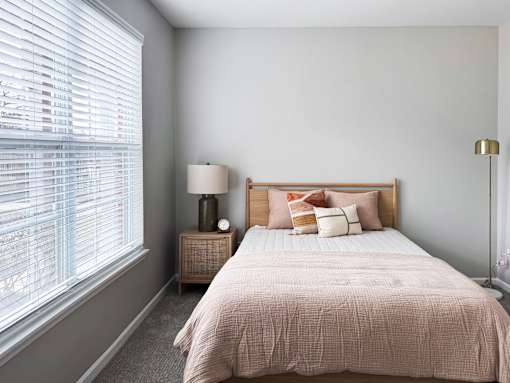 A bedroom with a bed, nightstand, and window with blinds.