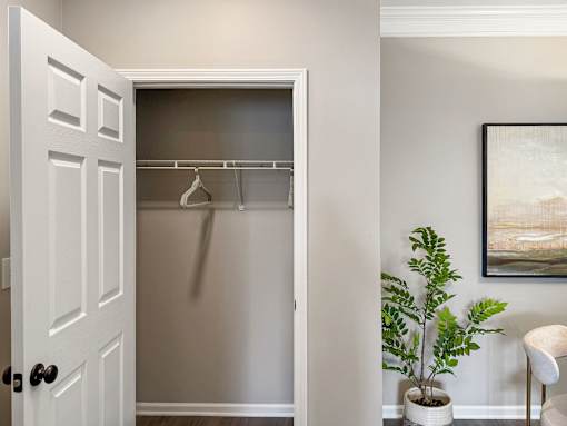 A white door with a black handle is open to a room with a plant and a painting.