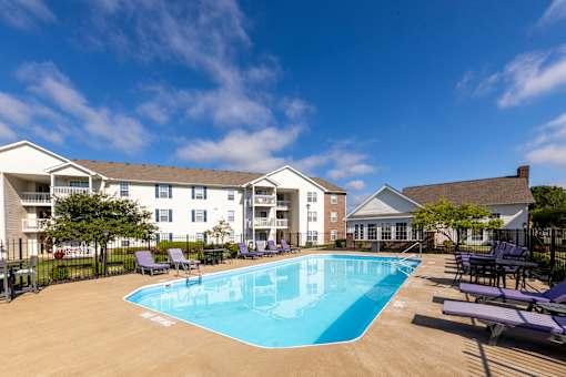 A swimming pool surrounded by lounge chairs and apartment buildings.
