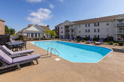 A pool surrounded by lounge chairs and apartment buildings.