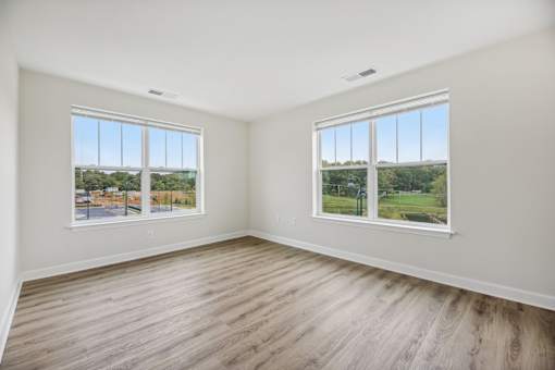 A room with two windows overlooking a street and a green field.