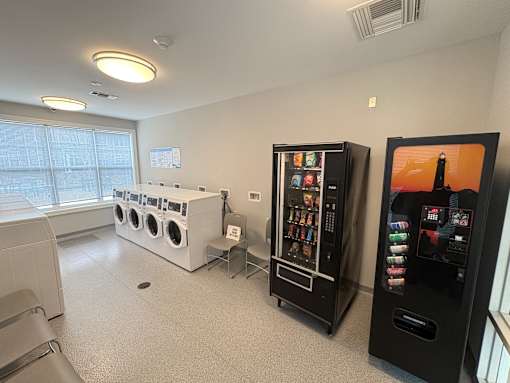 A room with a washing machine, a vending machine, and a fridge.