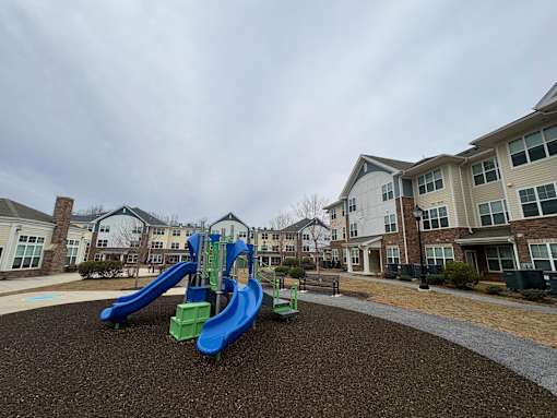 A playground with a blue and green slide in front of apartment buildings.