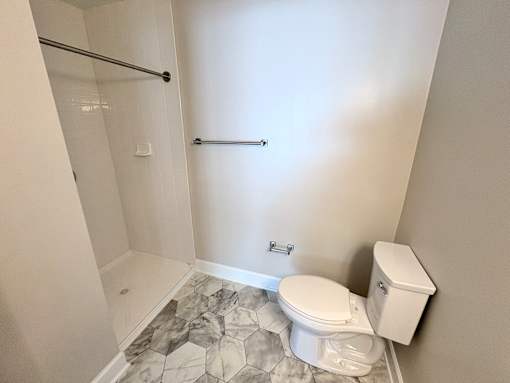 A white toilet sits next to a marble tiled floor in a bathroom.