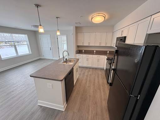A kitchen with a black refrigerator and wooden floors.