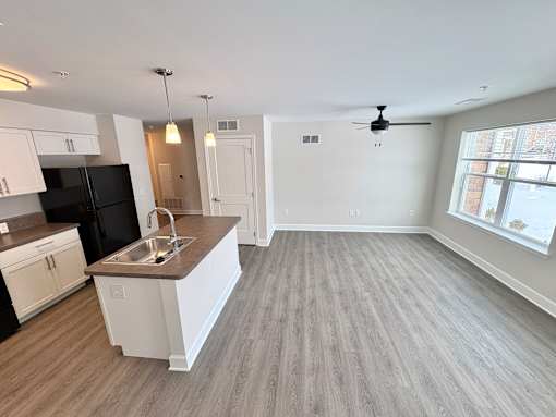 A spacious kitchen with a black refrigerator, white cabinets, and a wooden floor.