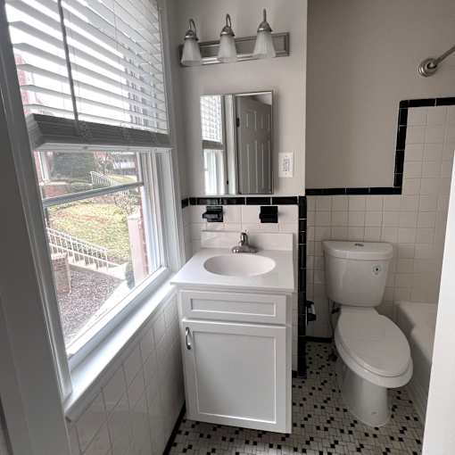 A white bathroom with a sink, toilet and window.
