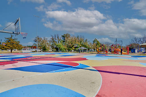 a basketball court with a playground and trees in the background