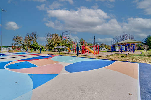 a basketball court with a playground and trees in the background