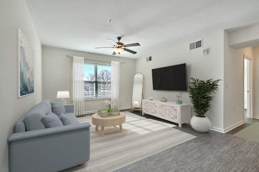 A living room with a grey couch, a coffee table, a television, and a ceiling fan.
