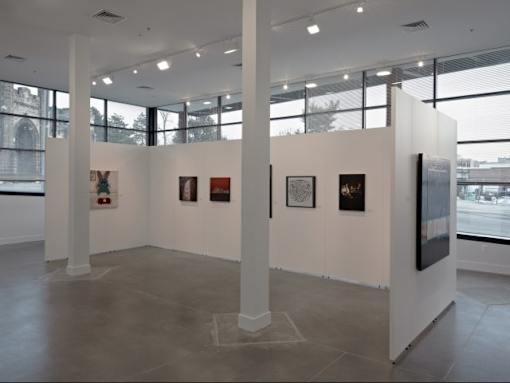 A gallery with white walls and a grey floor displays a collection of framed artwork.