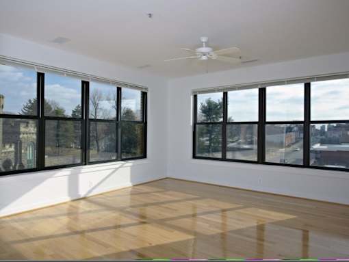 A room with a ceiling fan and large windows.