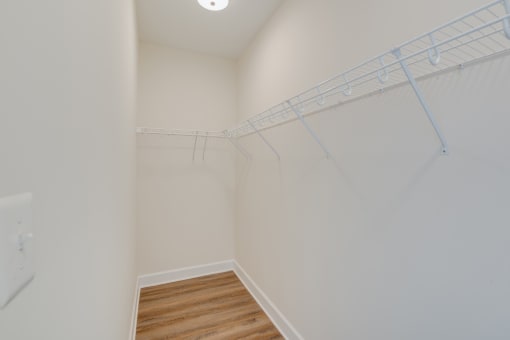 a walk in closet with white walls and a wooden floor