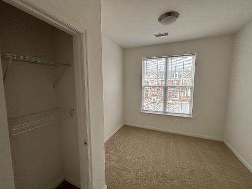 A small, empty room with a window showing a view of a residential area.