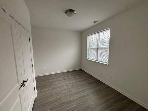A room with a wooden floor and a window with blinds.