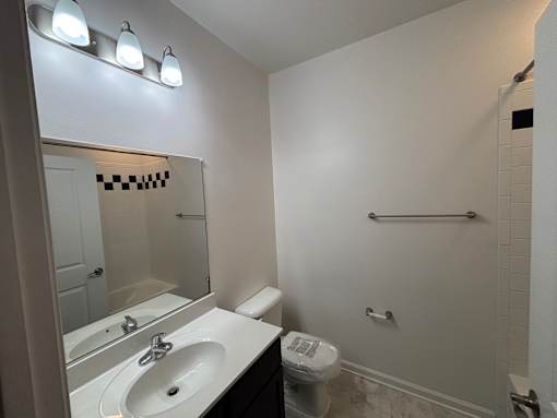 A bathroom with a sink, mirror, toilet, and a towel rack.