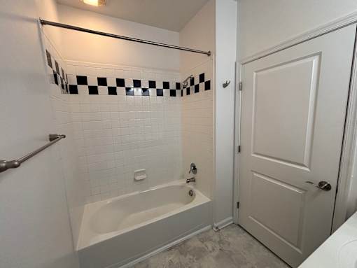 A white bathroom with a checkered tile border on the shower.
