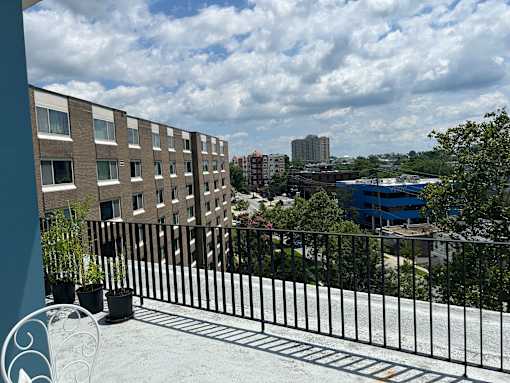 A balcony with a black railing and potted plants overlooks a cityscape.