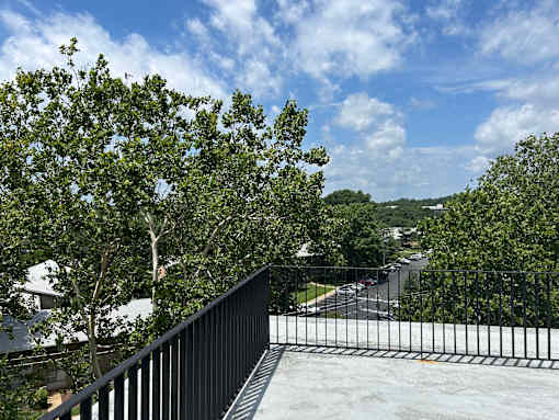 A balcony with a black railing overlooks a street with cars and houses.