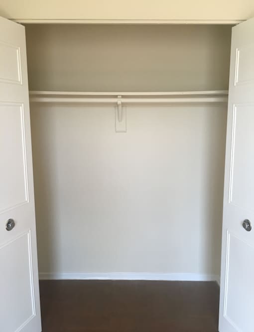 A white door is open to a room with a white wall and a brown floor.