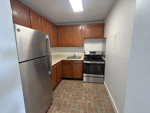 A kitchen with a stainless steel refrigerator, oven, and wooden cabinets.