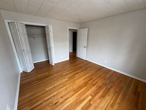 A room with wooden flooring and two doors, one open and one closed.