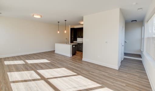 an empty living room with a kitchen in the background
