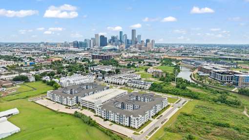 Apartment community exterior highlighting architectural design, structured parking, landscaped open areas, and a dynamic city backdrop.