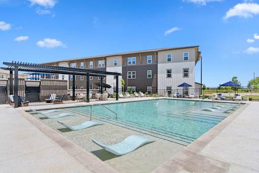 Pool at The Esther apartments in Converse, TX with tanning deck, lounge seating and umbrellas.