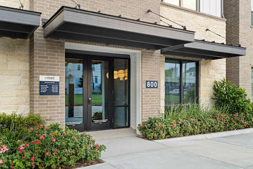 Apartment community leasing office entrance featuring contemporary architecture, landscaped grounds, covered pedestrian access, and a welcoming resident arrival experience.
