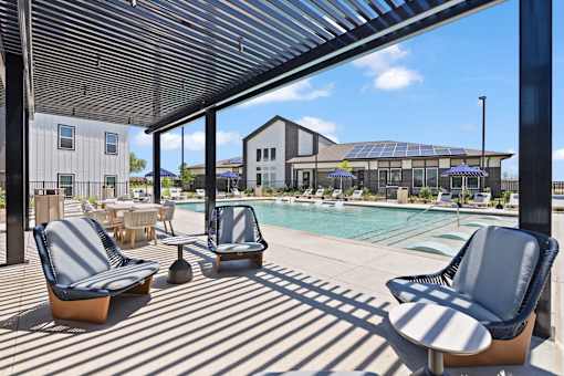 Pool at The Esther apartments in Converse, TX with tanning deck, lounge seating and umbrellas.